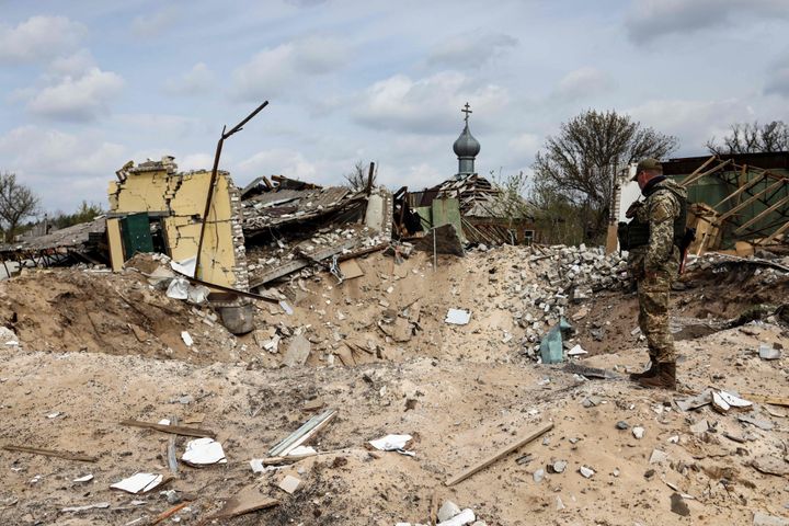 A Ukranian serviceman looks into a crater and a destroyed home are pictured in the village of Yatskivka, eastern Ukraine on April 16, 2022. - Russia's military focus now seems to be on seizing the eastern Donbas region, where Russian-backed separatists control the Donetsk and Lugansk areas. Lugansk governor Serhiy Gaidai called on April 16, 2022, for civilians to leave the area while they still can.