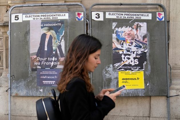 A woman walks in front of torn campaign posters of French President Emmanuel Macron and candidate for...