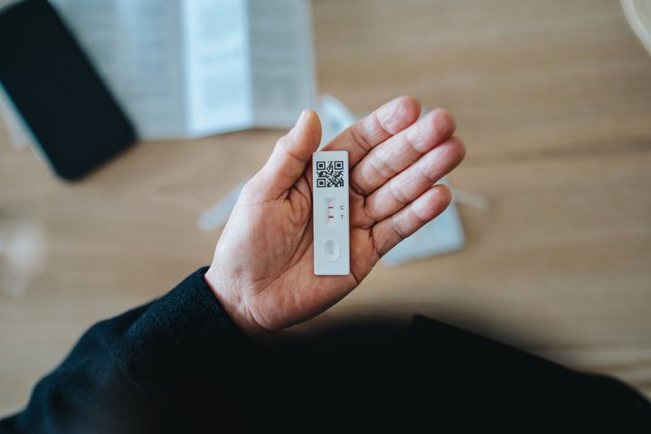 Overhead view of senior Asian woman carrying out a Covid-19 rapid lateral flow test at home. She is holding a positive Coronavirus rapid self test device, feeling worried