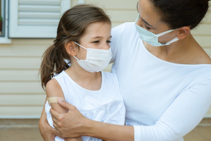 Child with protective face mask is sitting in her mothers lap. They are looking at eachother.