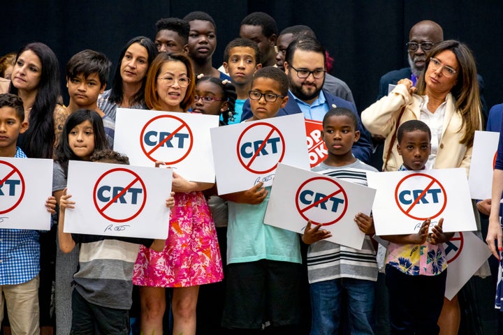 Kids holding signs against critical race theory stand onstage near Florida Gov. Ron DeSantis as he signs an anti-CRT bill.