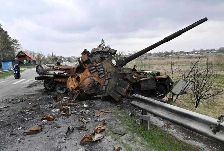 A man ride a motorbike past a destroyed Russian tank on a road in the village of Rusaniv, in the Kyiv region 