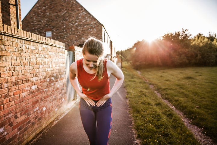 Sporty woman outdoors, holding her stomach in pain