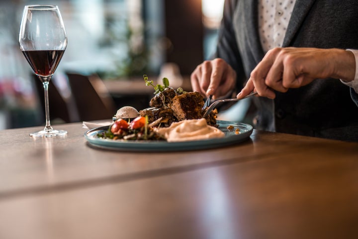 Hand close-up of elegant man having lunch and wine at a restaurant. Ribs, mashed potato, salad and cream.