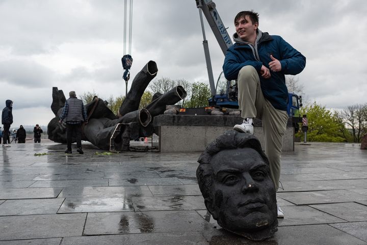 A young man poses with his foot on a head from the the "Friendship of Peoples" monument during its demolition on April 26, 2022, in Kyiv. 