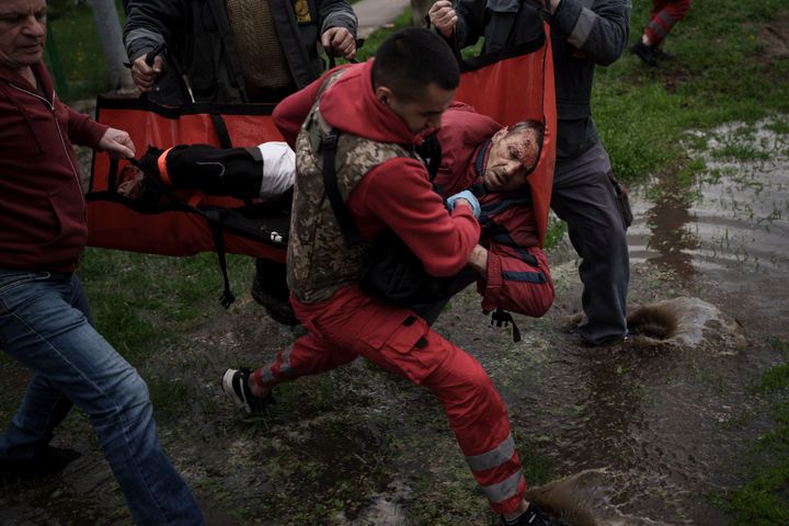 An emergency worker is helped by locals to carry a man to an ambulance following a Russian bombardment in Kharkiv, Ukraine, on April 27, 2022.