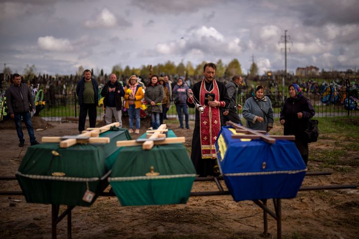 A priest blesses the remains of three people who died during the Russian occupation and were disinterred from temporary burial sites in Bucha, on the outskirts of Kyiv, on Wednesday, April 27, 2022. (AP Photo/Emilio Morenatti)