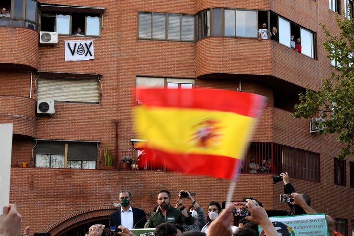 Acto de Vox en Vallecas. De fondo, una vecina se asoma junto a un cartel contra el partido de ultraderecha.