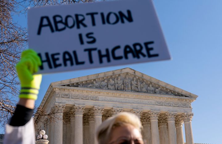 A woman in a doctors uniform holds a poster that reads "Abortion is Healthcare" as abortion rights advocates and anti-abortion protesters demonstrate in front of the U.S. Supreme Court on Dec. 1, 2021.