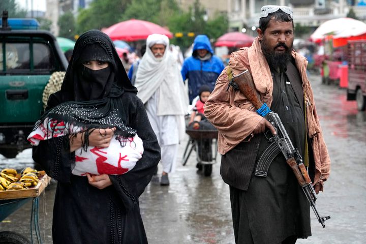 An Afghan woman walks through the Old Market as a Taliban fighter stands guard, in downtown Kabul, Afghanistan, Tuesday, May 3, 2022.