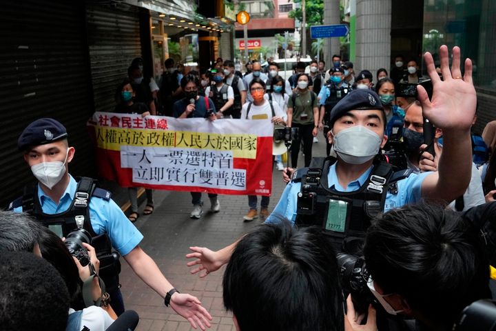 Οι διαδηλωτές υπέρ της δημοκρατίας περικυκλώνονται από αστυνομικούς καθώς φέρουν ένα πανό κατά των εκλογών του διευθύνοντος συμβούλου κοντά σε ένα εκλογικό τμήμα στο Χονγκ Κονγκ, Κυριακή 8 Μαΐου 2022. (AP Photo/Kin Cheung)
