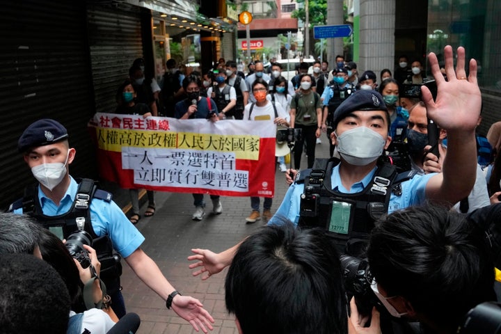 Pro-democracy protesters are surrounded by police officers as they carry a banner against the chief executive election near a polling station in Hong Kong, Sunday, May 8, 2022. (AP Photo/Kin Cheung)