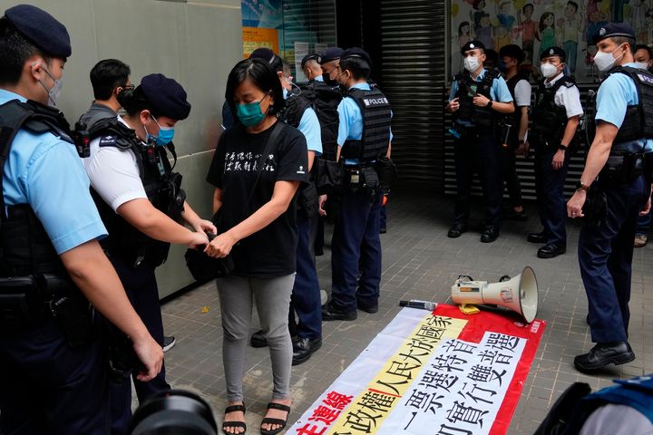 A pro-democracy protester is searched by police officers as she chants slogan against the chief executive election near a polling station in Hong Kong, Sunday, May 8, 2022. (AP Photo/Kin Cheung)