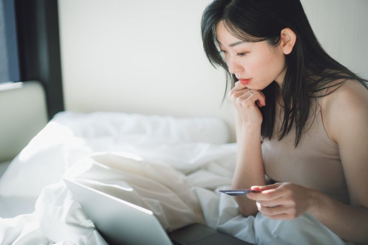 Shot of a young woman relaxing on the bed and using a credit card to shop online with a laptop
