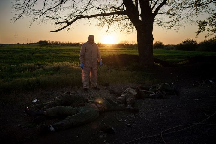 A Ukrainian emergency worker stands next to the bodies of Russian soldiers in the village of Vilkhivka, recently retaken by Ukrainian forces near Kharkiv, Ukraine, on May 9, 2022.