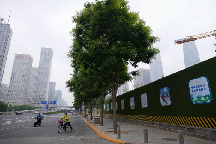 A delivery worker and a cyclist ride across a street in the central business district during what is normally the morning rush hour, as most nonessential workers in the district have been ordered to work from home in the Chaoyang district on May 10, 2022, in Beijing.