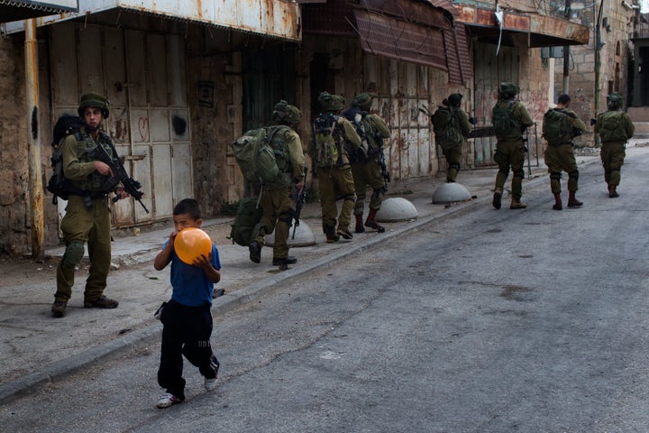 Un niño palestino infla un globo delante de soldados israelíes de patrulla por Hebrón, Cisjordania.