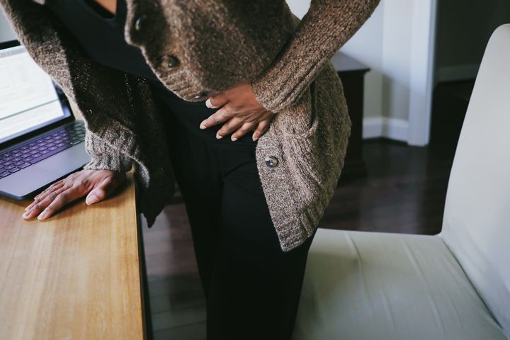 Close-up of unrecognizable black woman bending over desk in pain