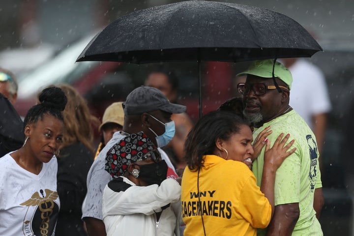 Bystanders gather under an umbrella as rain rolls in after a mass shooting at a supermarket in Buffalo, New York, Saturday.