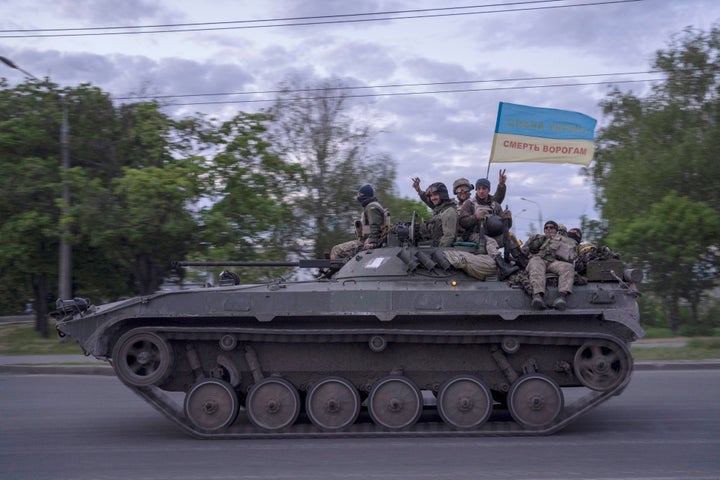 Ukrainian serviceman wave a flag with writing reading in Ukrainian "Glory to Ukraine," top, and "Death to the enemies" as they ride atop of a tank in the Kharkiv region, eastern Ukraine, on May 16, 2022.