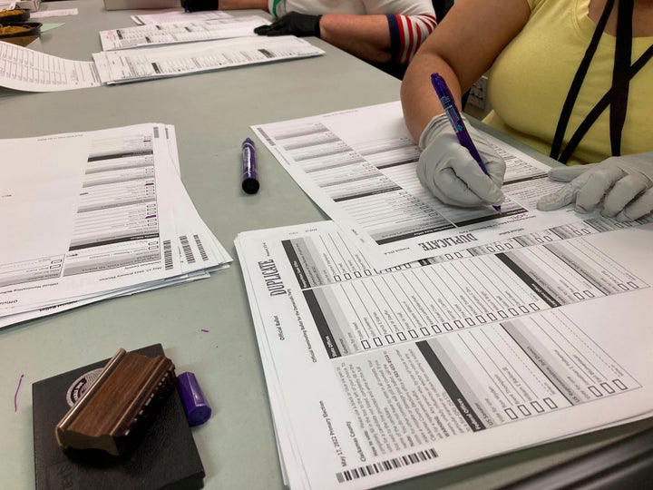 Workers check ballots at elections offices in Clackamas County, Oregon, the state's third-most populous county, on May 17, 2022. Many ballots in the county were printed with blurry barcodes, preventing them from being read by voting tabulation machines. Workers, one Democrat and one Republican per pair, are re-recording votes from the blurred ballots on new ballots so they can be read.