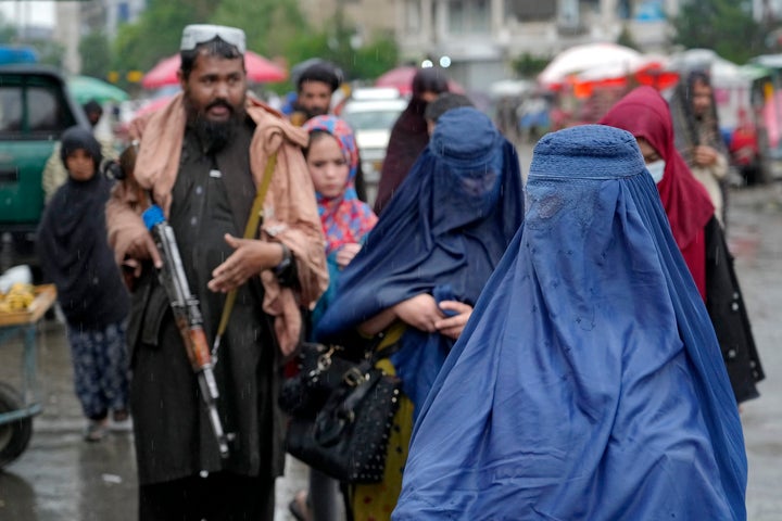 Covered women walk through a market as a Taliban fighter stands guard in the city of Kabul.