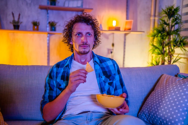 Young man watching a movie and eating snacks in the living room at night