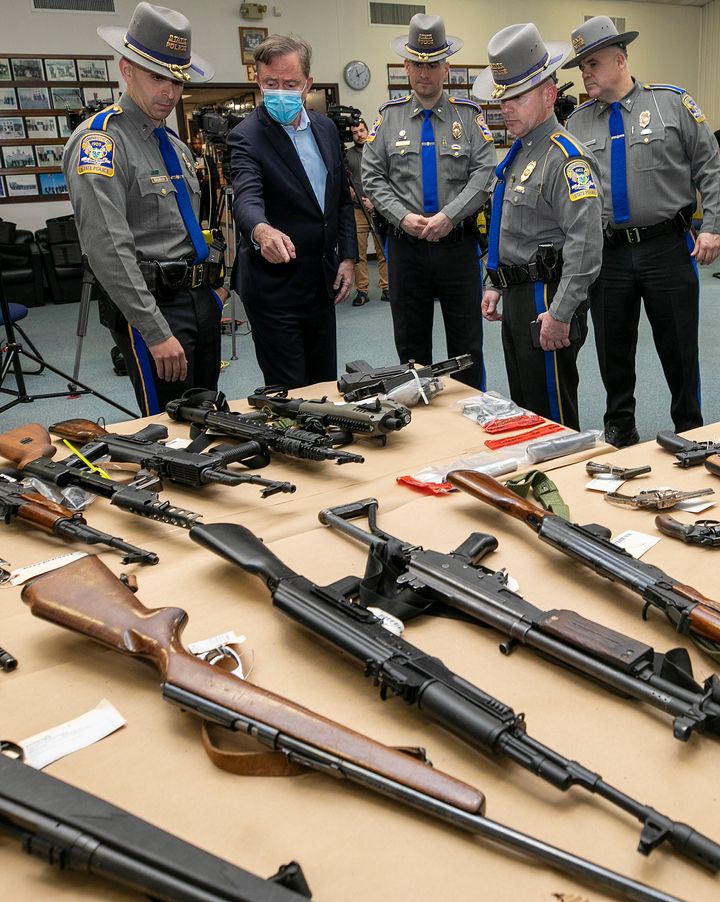 Gov. Ned Lamont and state troopers view dozens of assault weapons, rifles and handguns displayed on a table prior to a press conference at the Connecticut Forensic Science Laboratory in Meriden, Conn., on April 14, 2022.