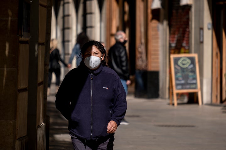 Una mujer camina por una calle con su mascarilla cubriendo la cara