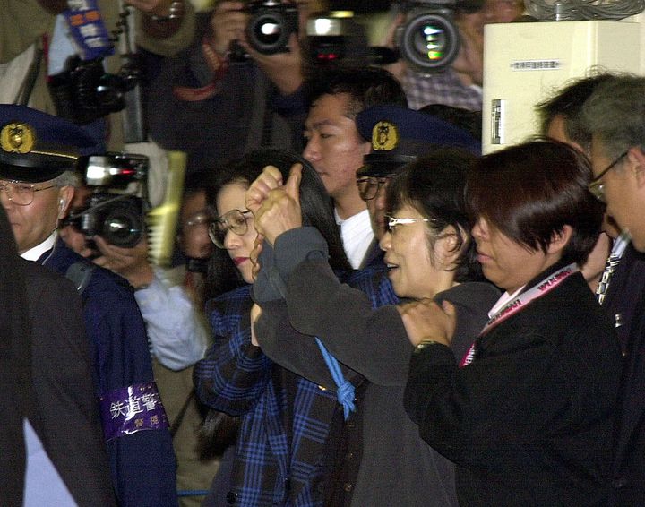Η Φουσάκο Σιγκενόμπου με χειρπέδες στα χέρια συνοδεύεται από αστυνομικούς κατά την άφιξή της στο σιδηροδρομικό σταθμό του Τόκιο το 2000.
