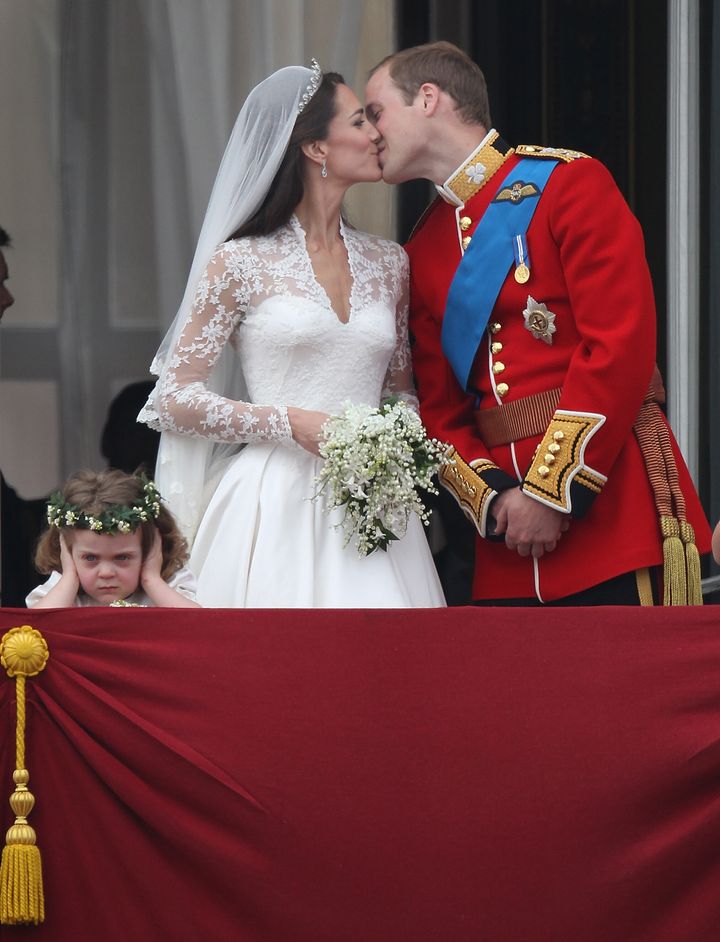 The Duke and Duchess of Cambridge kiss as bridesmaid Grace Van Cutsem looks at the crowd from the balcony at Buckingham Palace on April 29, 2011, in London.