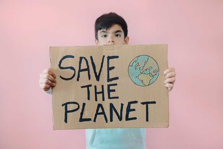 Young teenage boy holding a cardboard sign that says SAVE THE PLANET ..