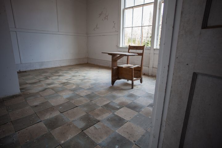 An antique wooden school desk sits in an empty classroom in an abandoned school.