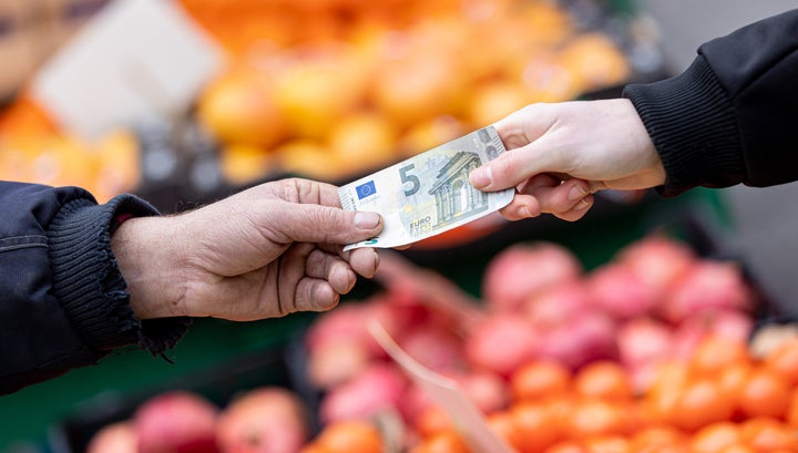 Dos personas agarrando un billete de 5 euros.