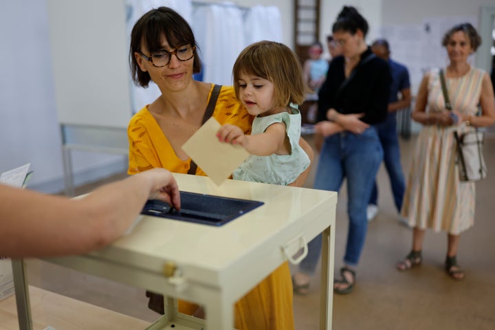 A girl casts the ballot for her mother at a voting station in Strasbourg, eastern France, Sunday June 12, 2022, Sunday, June 12, 2022. (AP Photo/Jean-Francois Badias)