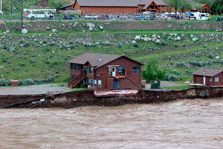In this image provided by Sam Glotzbach, the flooding Yellowstone River undercuts the river bank, threatening a house and a garage in Gardiner, Mont., on June 13, 2022. (Sam Glotzbach via AP)