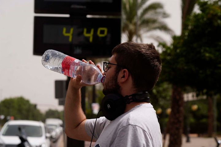 Un joven bebe agua junto a un termómetro de calle que marca 44º en el centro de Córdoba.