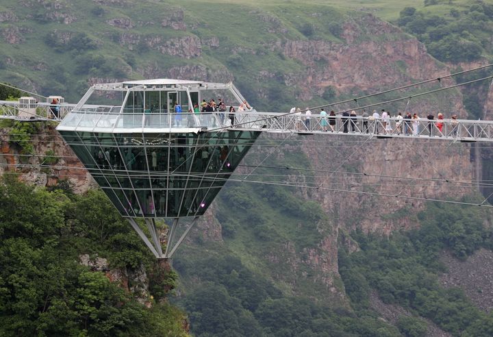 ダシュバシ峡谷に建設されたガラス製の吊り橋を渡る人々。ダイヤモンド型のカフェが見える（2022年6月14日撮影）