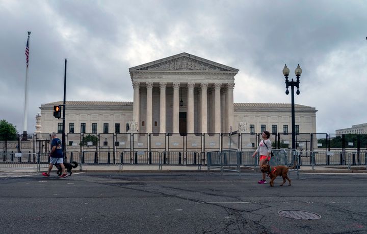 People walk dogs past anti-scaling fencing erected around the U.S. Supreme Court in Washington, on June 23, 2022.