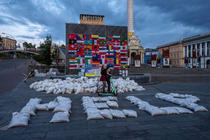 Women ride a scooter through Kyiv's Maidan Square, past sandbags that spell out 'HELP,' and flags displayed from around the world, in Ukraine, Saturday, June 25, 2022. (AP Photo/Nariman El-Mofty)