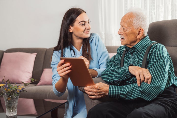 Supportive young female caregiver helping an elderly man at home. Nurse taking care of a senior male patient, examining his vitals.