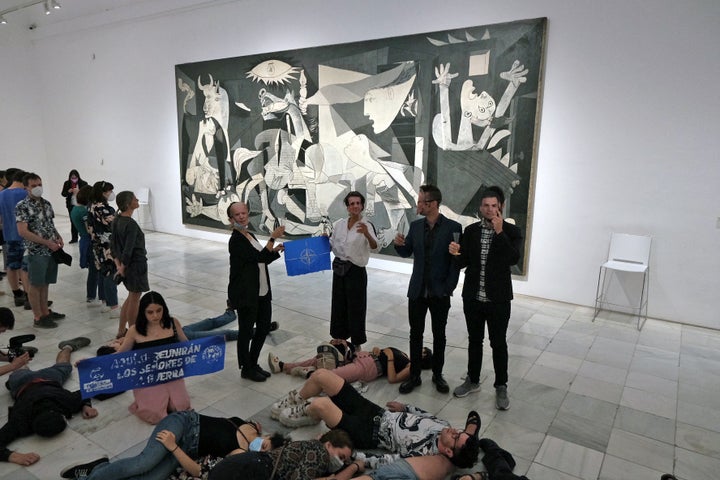 Extinction Rebellion activists wear masks with pictures of NATO leaders in front of Pablo Picasso's 'Guernica' painting at Reina Sofia museum during a protest against a NATO summit in Madrid, Spain, June 27, 2022. Extinction Rebellion/Aurele Castellane/Handout via REUTERS