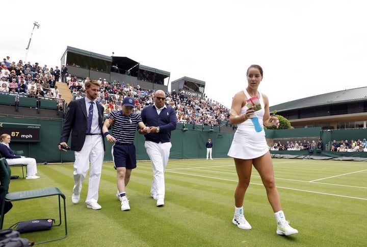 Britain's Jodie Burrage, right, walks back to her chair after giving a ball boy, second left, some refreshments after they fainted.