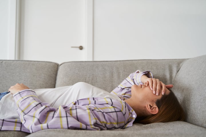 Unrecognizable young woman in casual clothes overwhelmed and stressed lying on the sofa in the living room of her home. Concept of mental health, anxiety and depression.