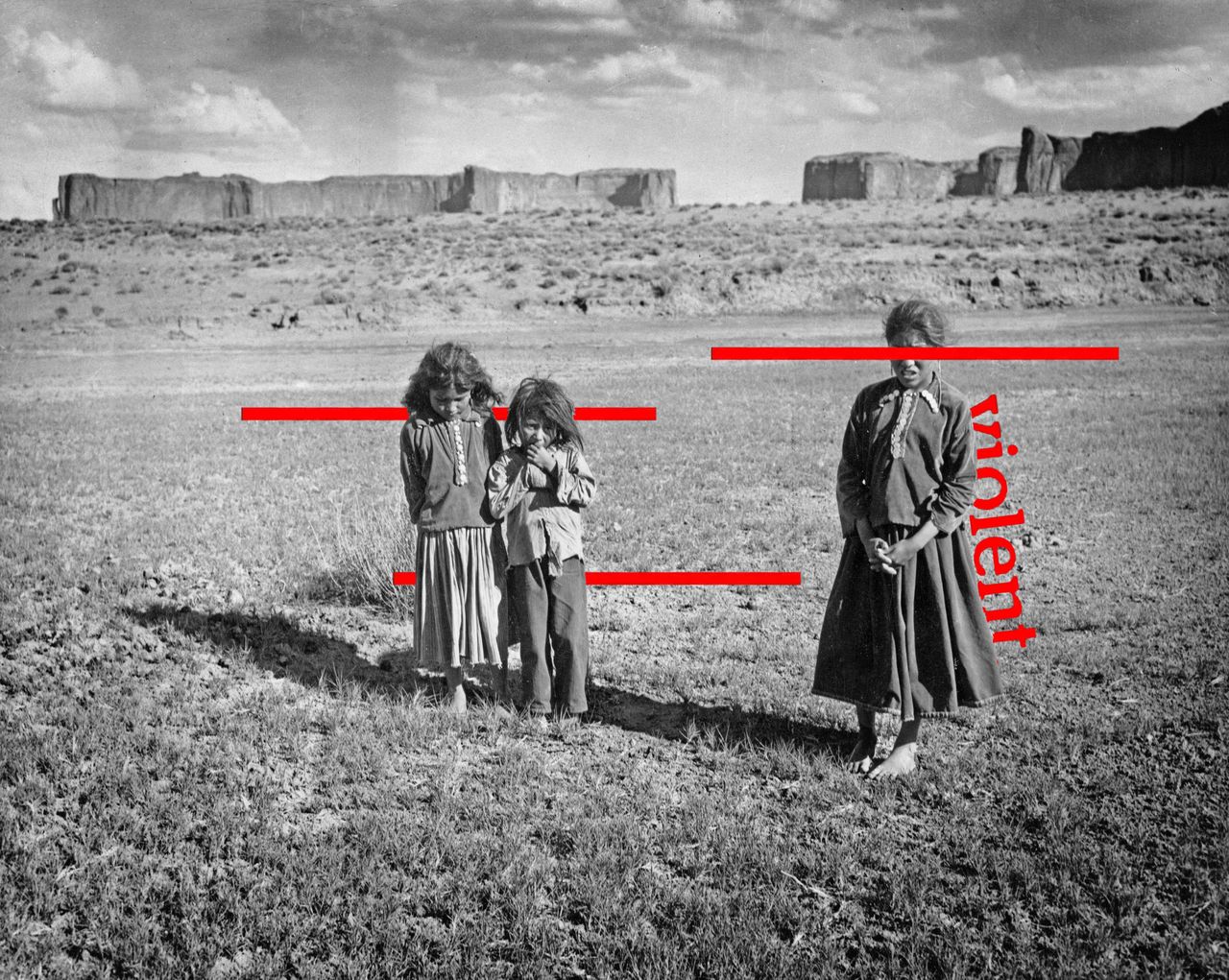 Three Navajo children, dressed in traditional clothing, stand barefoot in the grass against the rugged landscape of an unspecified Navajo reservation, United States, circa 1935.
