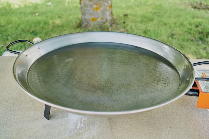 A paella pan with water is putted on a metallic burner before preparing the paella. A paella pan and some water inside it, all putted over a burner