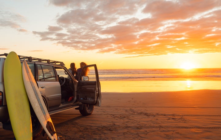 Two female friends enjoying sunset after the full day surfing on the beach.