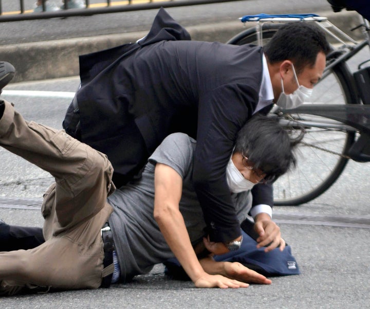 Tetsuya Yamagami, en bas, est détenu près du site des coups de feu dans la préfecture de Nara, dans l'ouest du Japon, le 8 juillet 2022.