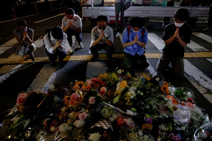 Aνθρωποι προσεύχονται δίπλα σε λουλούδια στην τοποθεσία όπου πυροβολήθηκε ο εκλιπών πρώην πρωθυπουργός της Ιάπωνας Σίνζο Άμπε κατά την εκστρατεία για βουλευτικές εκλογές, κοντά στο σταθμό Yamato-Saidaiji στη Νάρα, δυτική Ιαπωνία, 8 Ιουλίου 2022.