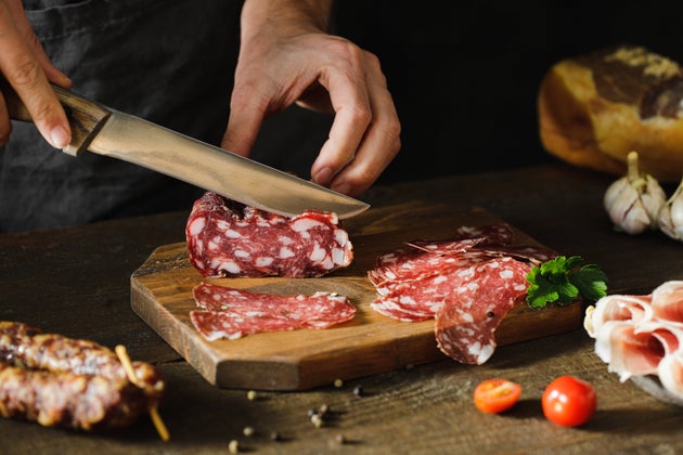 Close-up of a woman hands cuts salami sausage on wooden board. Female hands preparing cheese and meat platter on wooden kitchen table.